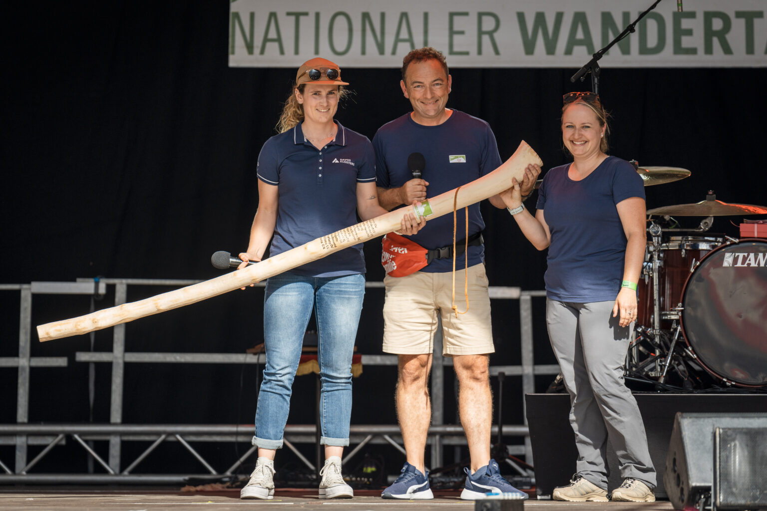 Chefredaktor Peter Jost und Corinne Müller von Willisau Tourismus (r.) übergeben den Wanderstock an Sara Koller von Davos Klosters Tourismus.