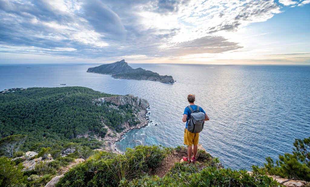 2PKHRHP Hiker looking into the distance, view of mountains and coast with sea, in the evening light, hiking to La Trapa from Sant Elm, in the back island Sa