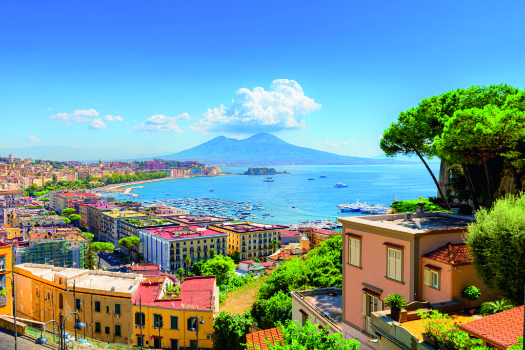 Naples, Italy. View of the Gulf of Naples from the Posillipo hill with Mount Vesuvius far in the background and some pine trees in foreground. August 31, 2021.